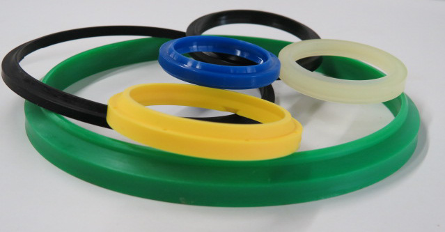 Assorted snap-in wiper seals in multiple sizes and colors, including green, yellow, blue, black, and translucent polyurethane rings, displayed on a white background